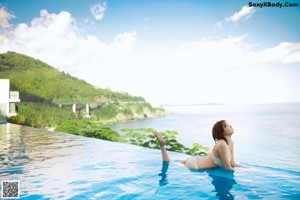 A woman sitting on a rock by the water.
