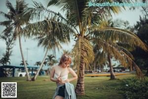 A woman in a bikini standing next to a palm tree.