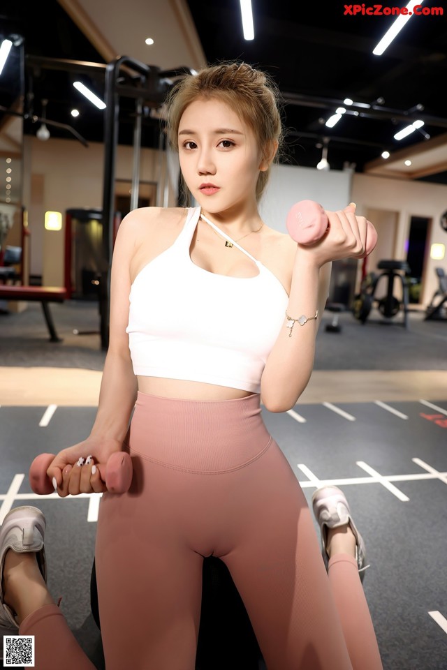 a woman in a white top and pink leggings holding two pink dumbbells