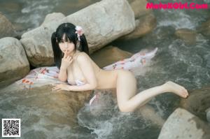 A woman in a pink kimono sitting on a rock by the water.