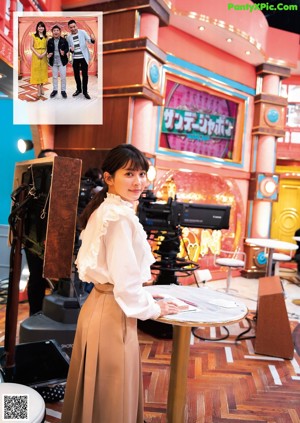 A woman in a white dress standing by a window.