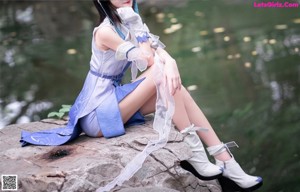 A woman in a blue and white outfit sitting on a rock.