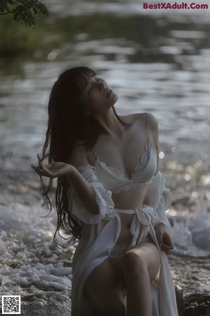 A woman in a white dress standing in the woods.