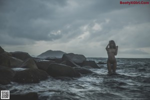 A naked woman sitting on a rock in the woods.