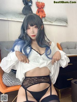 A woman with blue hair and glasses laying on a couch.