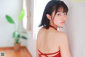 A woman in a red bathing suit leaning against a wall.